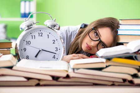 Young female student preparing for exams with many books in timeの写真素材