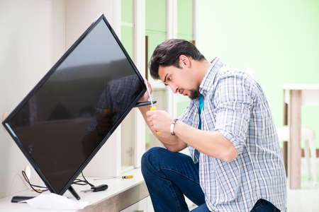 Young man husband repairing tv at homeの写真素材
