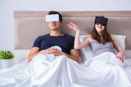 Wife and husband with virtual reality goggles in the bed