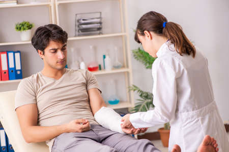 Young man with bandaged arm visiting female doctor traumatologisの写真素材