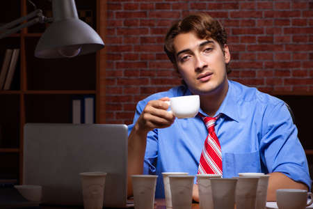 Young employee drinking coffee working at night shiftの写真素材