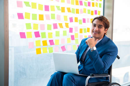 Young handsome man in wheelchair with many conflicting prioritieの写真素材