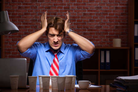 Young employee drinking coffee working at night shiftの写真素材