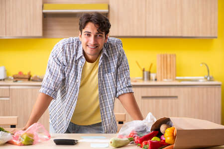 Young man calculating expences for vegetables in kitchenの写真素材