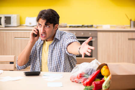 Young man calculating expences for vegetables in kitchenの写真素材