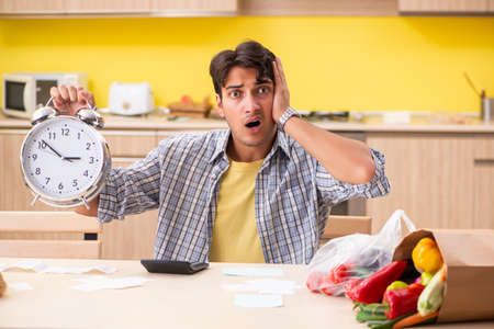 Young man calculating expences for vegetables in kitchenの写真素材