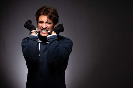 Young gangster in hood on grey background
