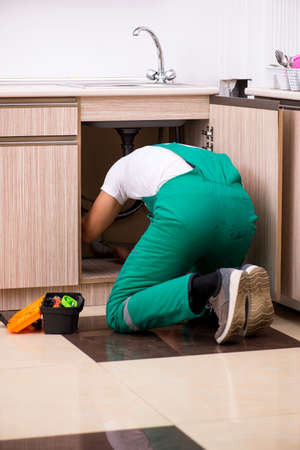 Young plumber repairing wash basin at kitchenの写真素材
