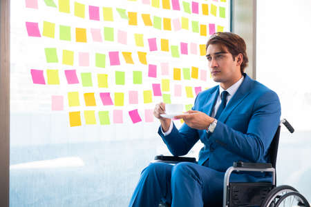 Young handsome man in wheelchair with many conflicting prioritieの写真素材