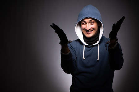 Young gangster in hood on grey background
