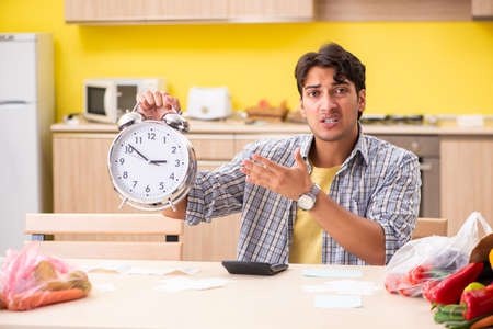 Young man calculating expences for vegetables in kitchenの写真素材