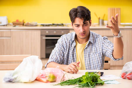 Young man calculating expences for vegetables in kitchenの写真素材