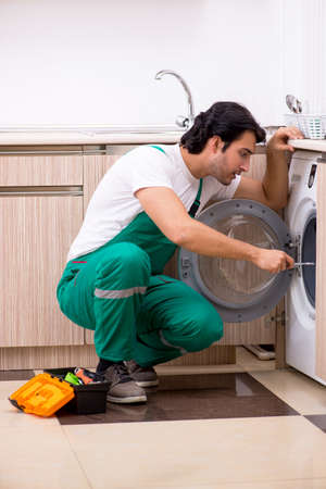 Young contractor repairing washing machine in kitchenの写真素材
