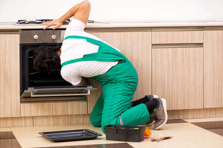 Young contractor repairing oven in kitchenの写真素材