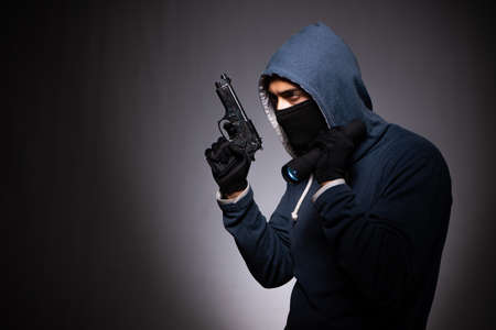 Young gangster in hood on grey background