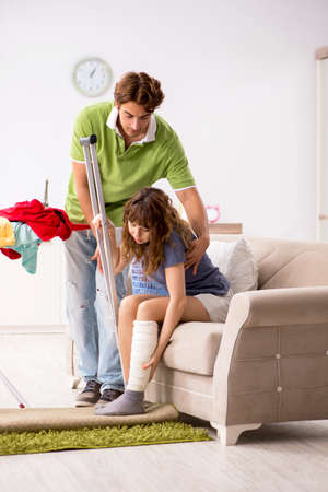 Husband helping leg injured wife in houseworkの写真素材
