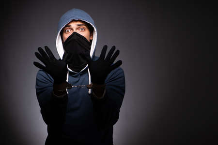 Young gangster in hood on grey background