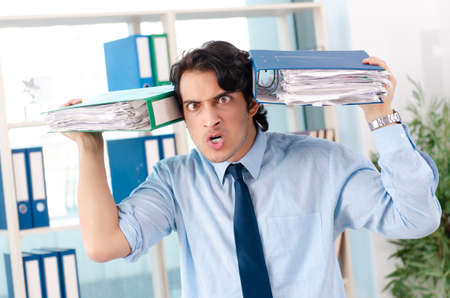 Young handsome male employee with too much work in the office