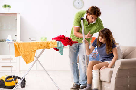 Husband helping leg injured wife in houseworkの写真素材