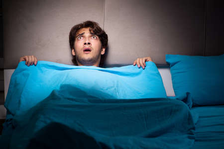 Young man scared in his bed having nightmaresの写真素材