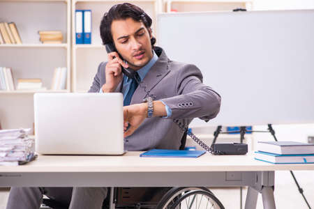 Young handsome employee in wheelchair at the officeの写真素材