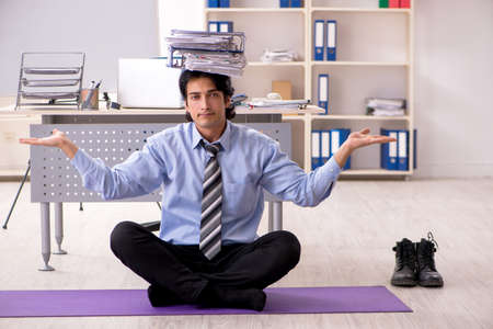 Young handsome male employee doing exercises in the officeの写真素材