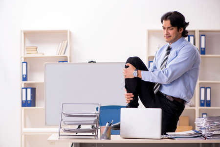 Young handsome male employee doing exercises in the officeの写真素材