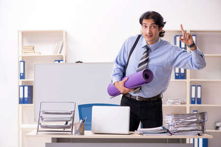 Young handsome male employee doing exercises in the officeの写真素材