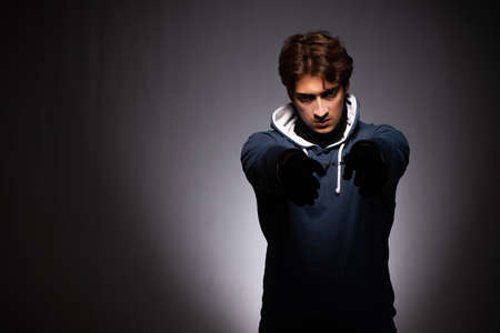 Young gangster in hood on grey background