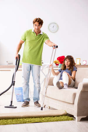 Husband helping leg injured wife in houseworkの写真素材