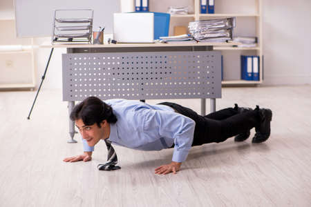 Young handsome male employee doing exercises in the officeの写真素材