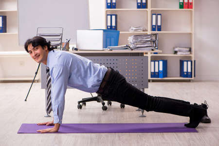 Young handsome male employee doing exercises in the office