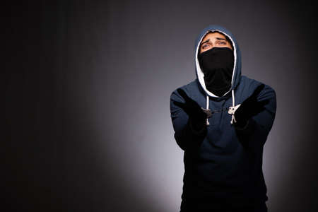 Young gangster in hood on grey background