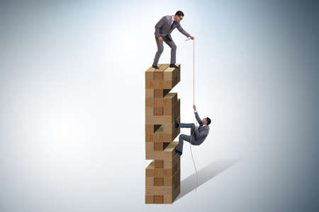Businessman helping colleague with ropeの写真素材