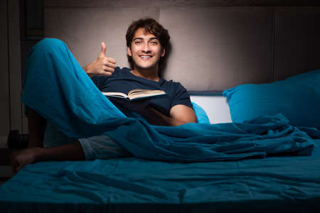 Young student reading book in bedの写真素材