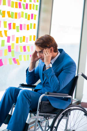 Young handsome man in wheelchair with many conflicting prioritieの写真素材