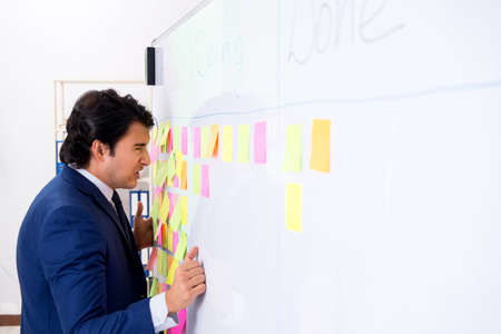 Young handsome employee in front of whiteboard with to-do listの写真素材