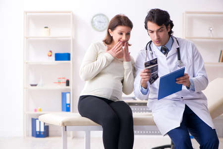 Old pregnant woman visiting young male doctorの写真素材