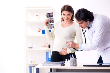 Old pregnant woman visiting young male doctorの写真素材
