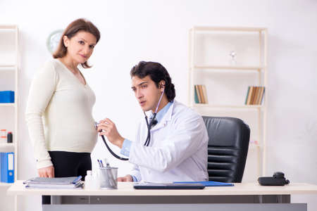 Old pregnant woman visiting young male doctorの写真素材