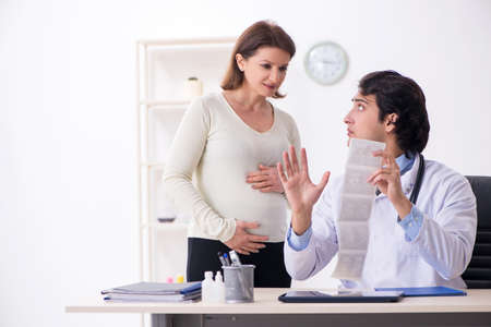 Old pregnant woman visiting young male doctorの写真素材
