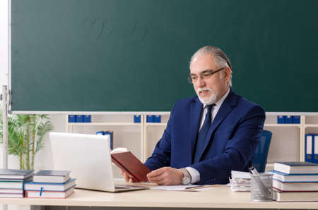 Aged male teacher in front of chalkboard