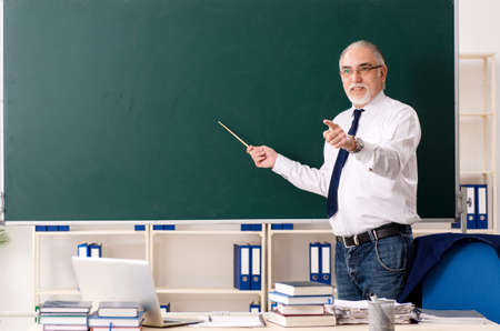 Aged male teacher in front of chalkboard