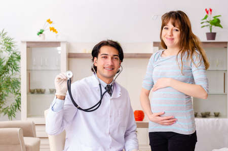 Young handsome doctor visiting pregnant woman at homeの写真素材