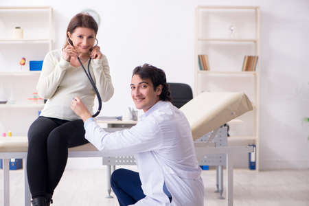 Old pregnant woman visiting young male doctorの写真素材