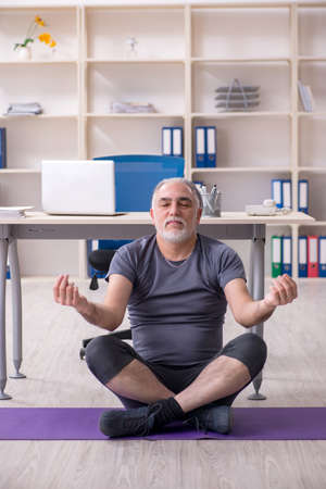 White bearded old man employee doing exercises in the officeの写真素材