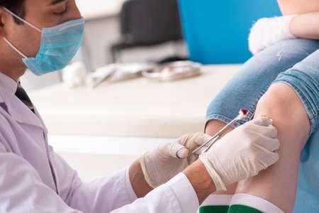 Leg injured young woman visiting male doctorの写真素材