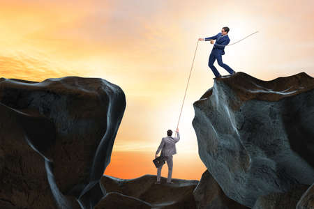 Businessman helping colleague with ropeの写真素材