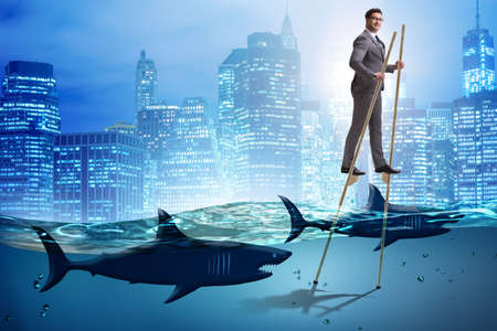 Businessman walking on stilts among sharksの写真素材