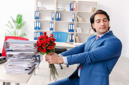 Young male employee with bunch of flowers in the officeの写真素材